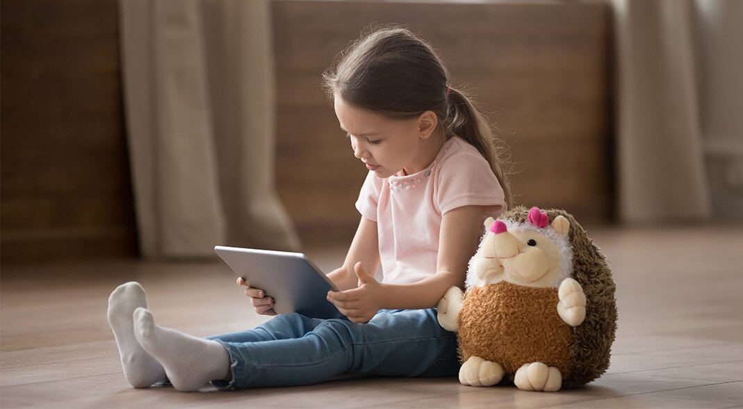 Ein kleines Mädchen sitzt auf dem Boden, mit einem Tablet auf dem Schoß | © iStock/fizkes